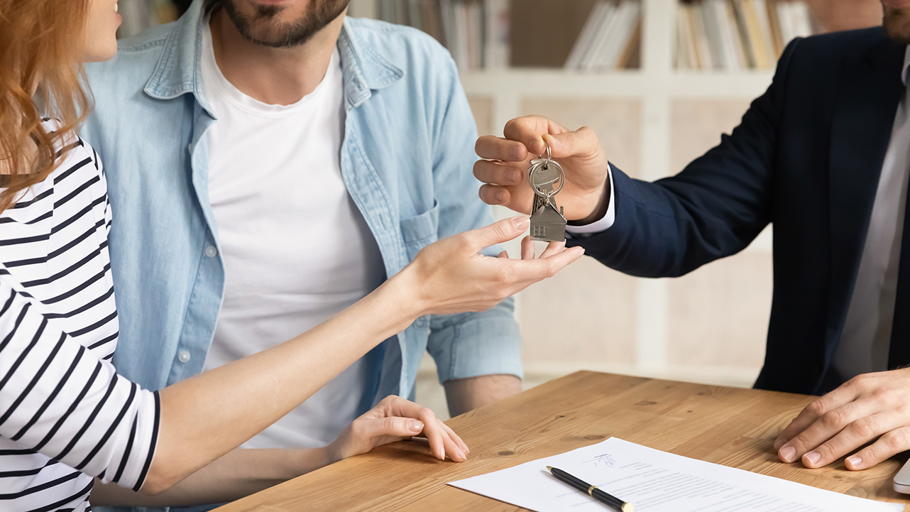 A couple receiving house keys from a professional, with documents on the table.