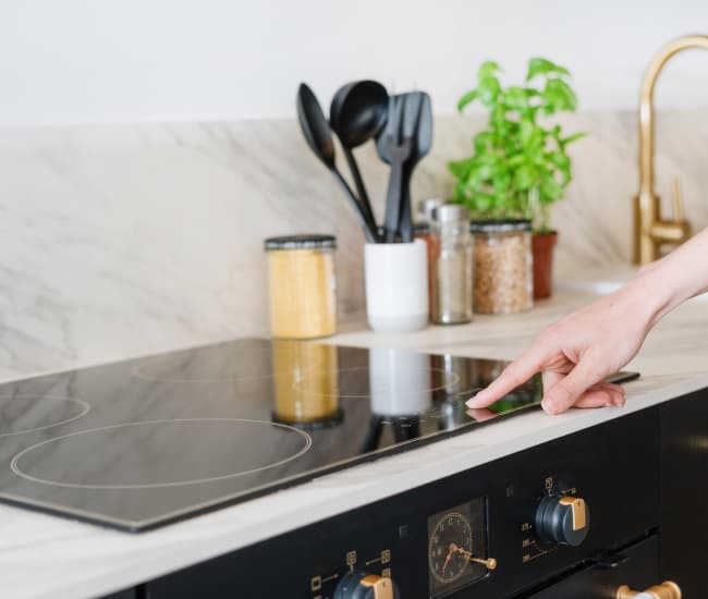 Close-up of someone using a sleek black induction cooktop with touch controls.