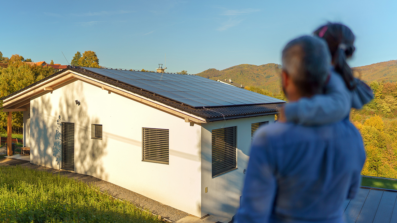 Father and child looking at a house equipped with solar panels on the roof.