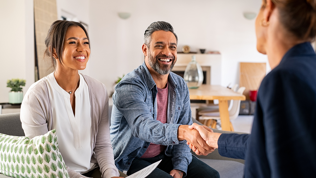 A couple discussing home improvement options and shaking hands with a professional indoors.